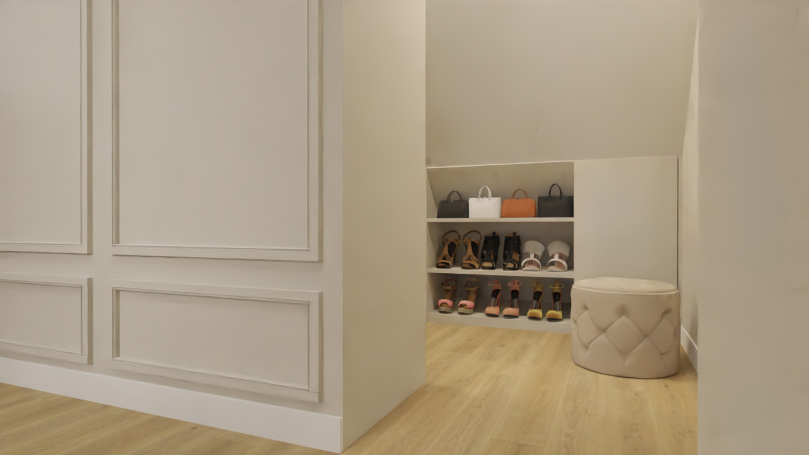 Slaapkamer inloopkast Lichte ruimte met open kast vol schoenen en een rond poefje aan de zijkant.
